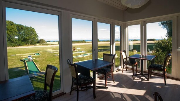 Habitación luminosa con ventanas amplias, una mesa y sillas, con vistas a un campo verde.