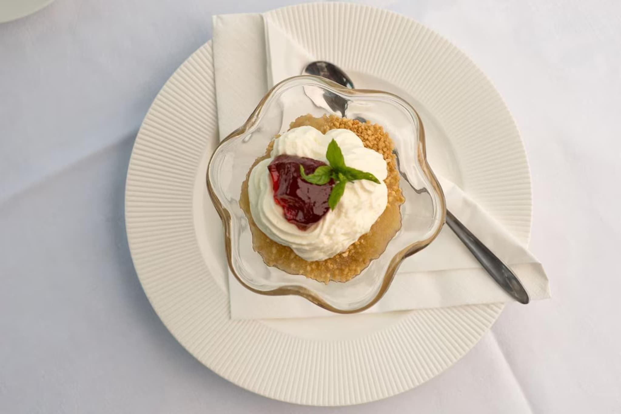En dessert på en hvid tallerken med ske og serviet.