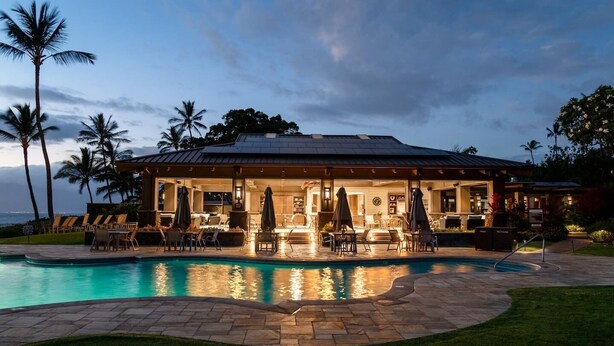 Une maison avec une piscine, un espace salon extérieur et des palmiers.