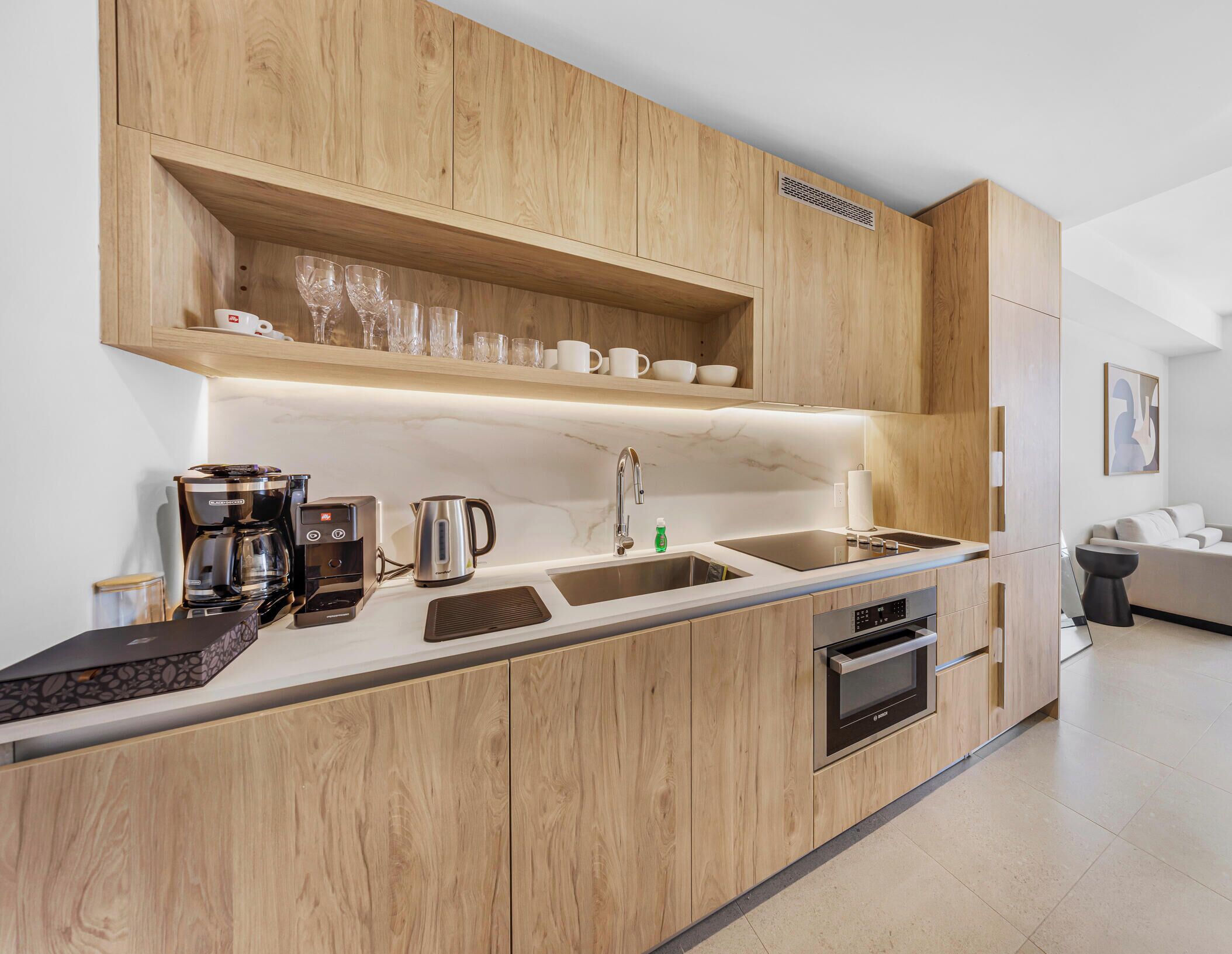 A modern kitchen with wooden cabinetry, a built-in oven, a coffee maker, and a kettle.