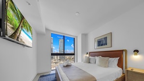 Habitación de hotel con cama, televisor montado en la pared, ventana grande con vista a la ciudad y un cuadro enmarcado.