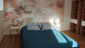 Een slaapkamer met een bed, nachtkastje, een wandlamp en een houten garderobe.