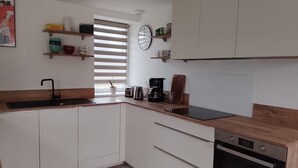 Een kleine keuken met witte kastjes, een zwarte gootsteen, een broodrooster, een koffiezetapparaat en een klok aan de muur.