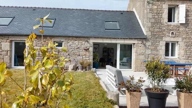 Een gebouw van steen met een schuin dak, een overdekte patio en een kleine tuin met potplanten.