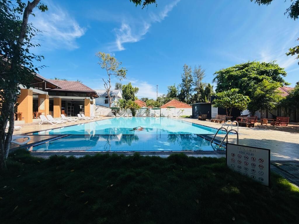 Una piscina con sillones reclinables, un cartel con símbolos y edificios al fondo.