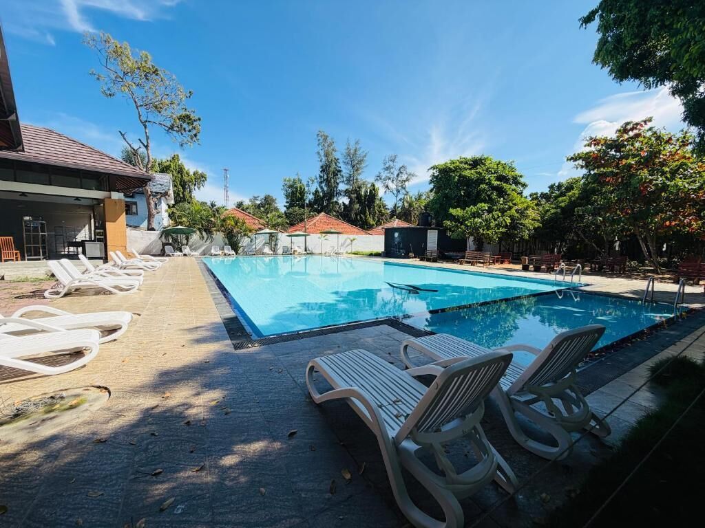 A swimming pool with lounge chairs, a covered area, and a building with a tiled roof.