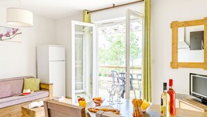 Una habitación con una mesa de comedor, sillas, un sofá, una televisión y un ventanal con vista a zonas verdes.