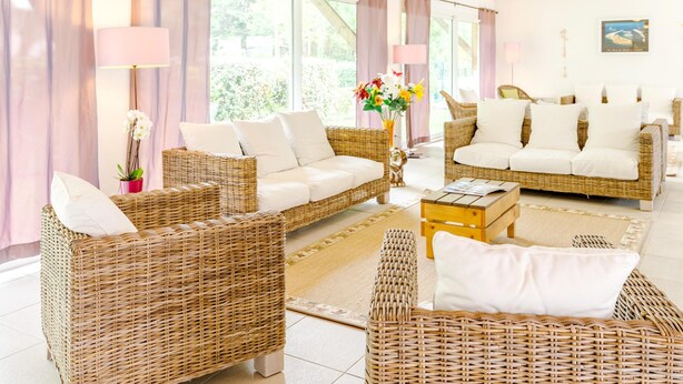 Una habitación con muebles de mimbre, una mesa de centro y ventanas amplias con cortinas.
