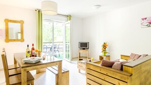 Una habitación con una mesa de comedor de madera, sillas, un sofá, un televisor y una ventana con cortinas.