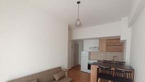 A compact living space with a sofa, a small table, a kitchenette, and a dining area with chairs.