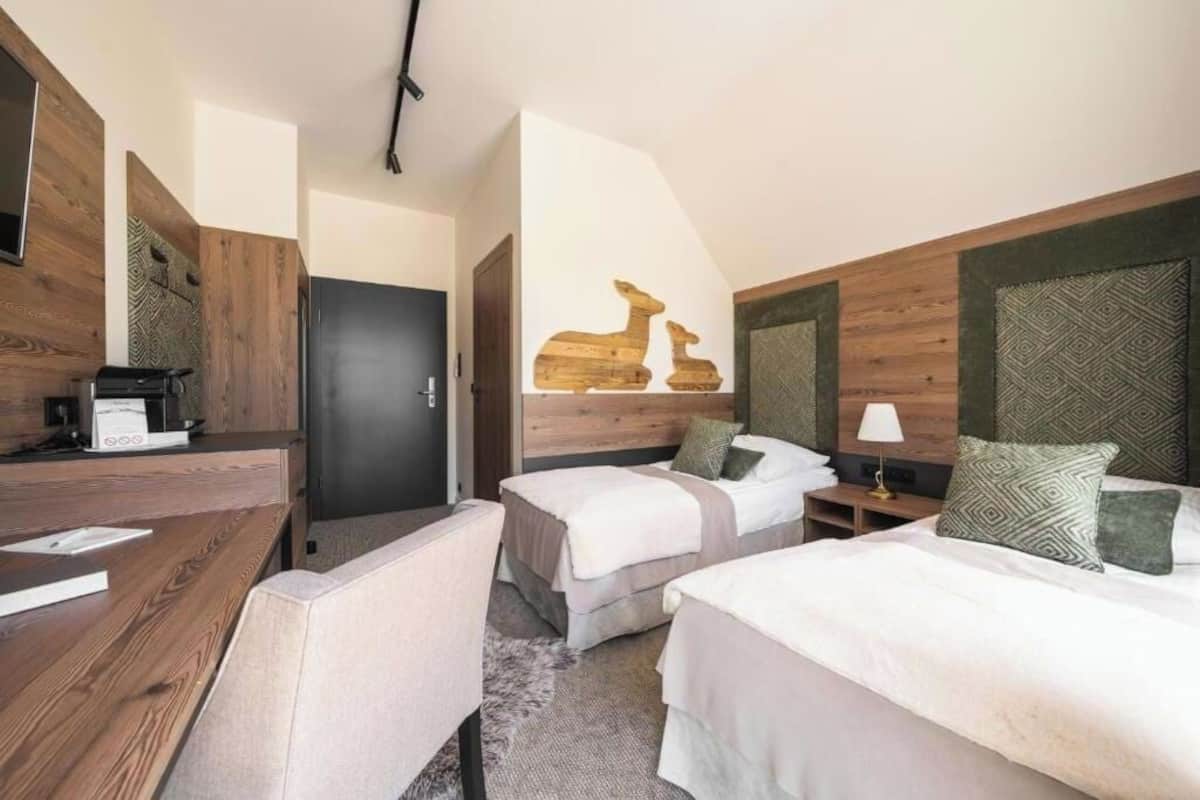 A hotel room with two beds, a desk, a coffee machine, and a door.
