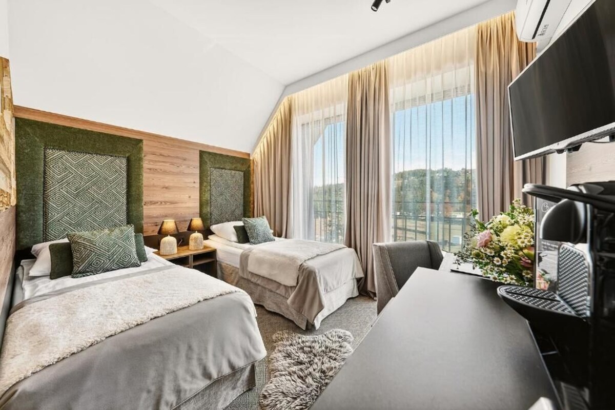 Una habitación de hotel con dos camas, un escritorio, un televisor y un ventanal con cortinas.