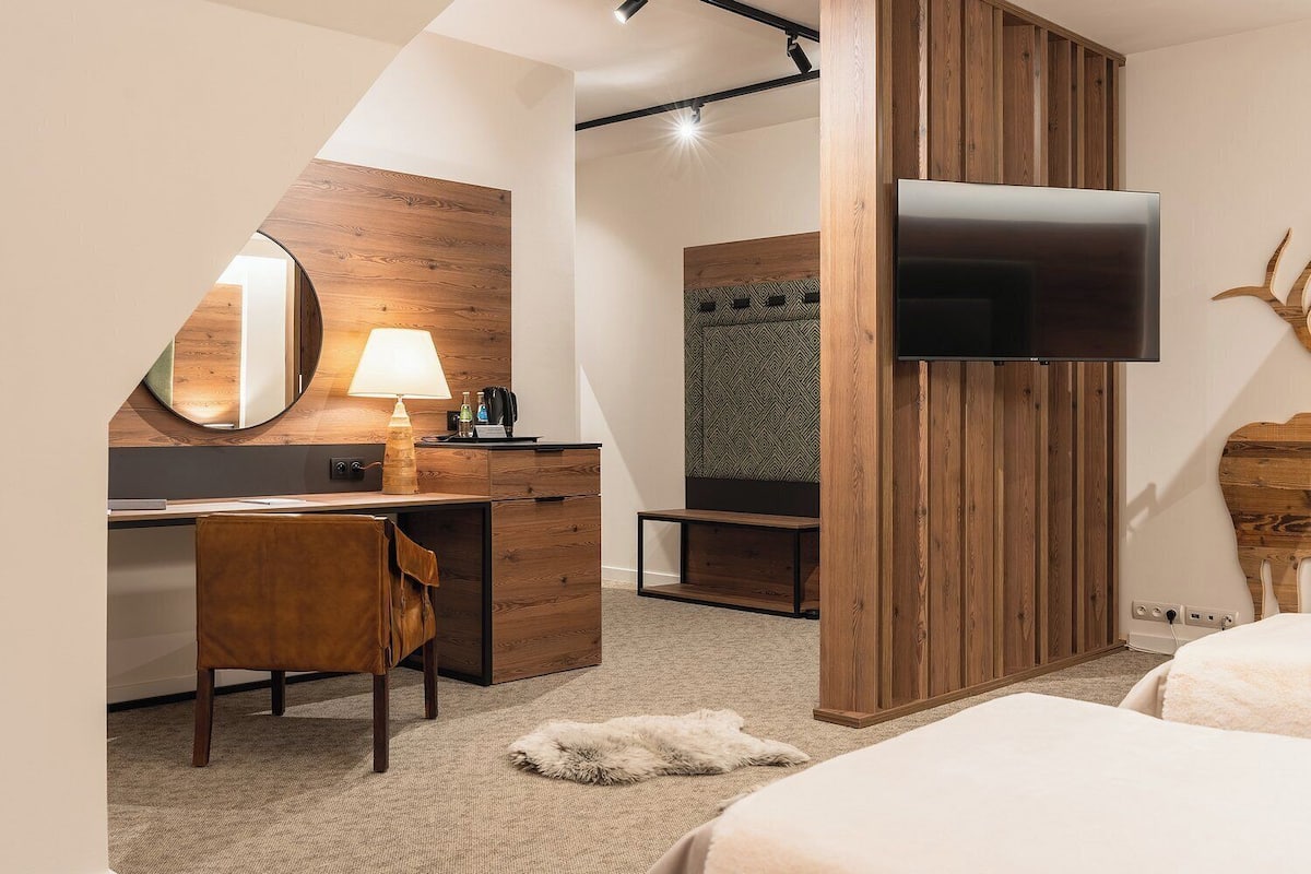 A modern hotel room with a desk, chair, bed, and a mounted TV.