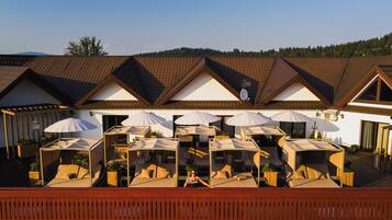 A hotel with outdoor seating areas, multiple umbrellas, and a view of a forested hill.