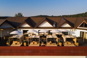 A hotel with outdoor seating areas, multiple umbrellas, and a view of a forested hill. - Termy Szaflary (Szaflary)