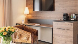 Hotelkamer met een bureau, een aan de muur bevestigde televisie, een lamp, een koffiezetapparaat en een bloemenvaas.