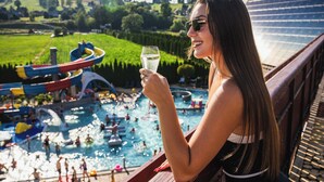 A person holding a glass of water, overlooking a swimming pool with people and water slides. - Termy Szaflary (Szaflary)