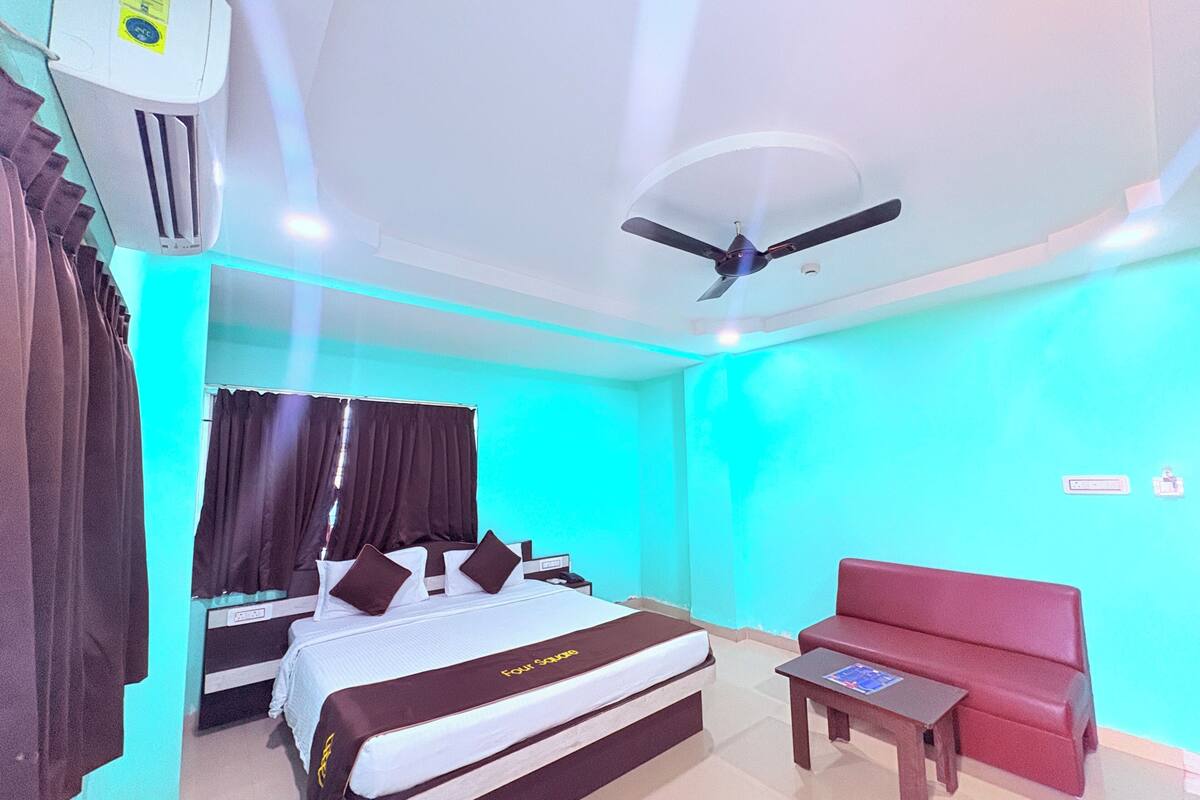 Una habitación de hotel con una cama, un sofá rojo, una mesita y un ventilador de techo, además de un equipo de aire acondicionado.