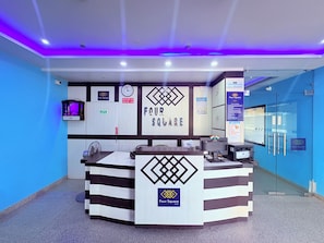 Un mostrador de recepción con el logotipo de Four Square Lite, un reloj y una puerta de vidrio con barra de empuje.