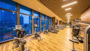 A gym with cardio machines, weight stations, and large windows offering a city view.