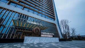 A modern hotel with a prominent glass facade, a large circular sculpture in front, and signage indicating it is 'The Cube Hotel'.