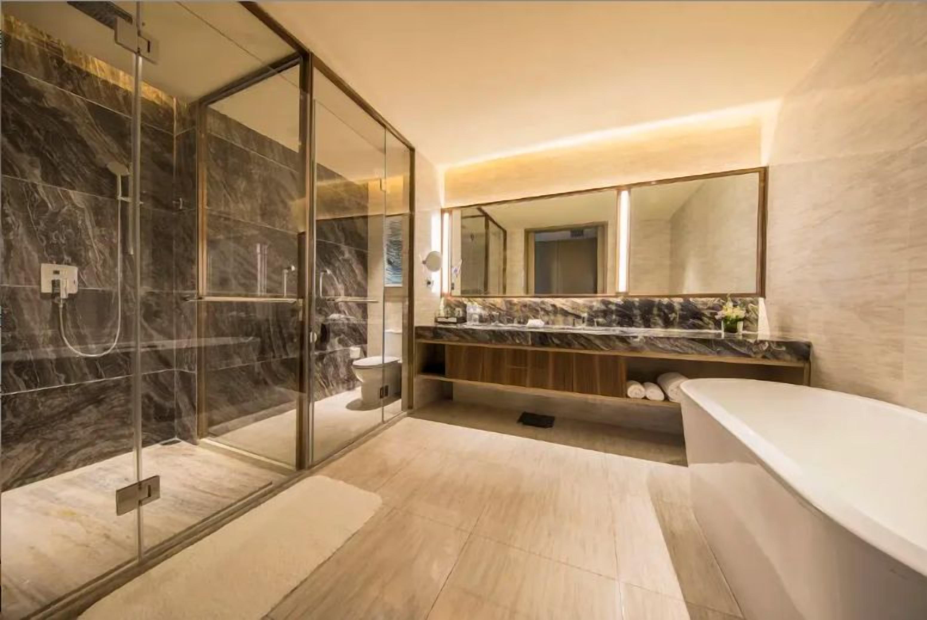 A modern bathroom with a glass-enclosed shower, a large mirror, and a marble countertop.