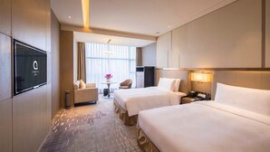 A hotel room with two beds, a TV, a desk, and a window with curtains.