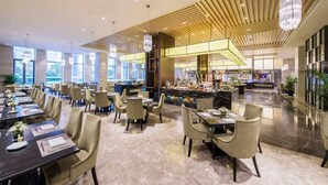 A spacious hotel lobby with a central bar area, multiple seating arrangements, and large windows allowing natural light.
