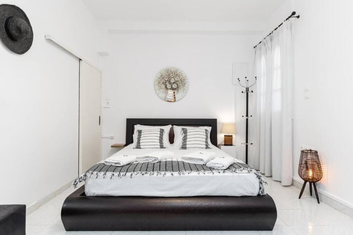 A modern bedroom with a large bed, a wall-mounted clock, a coat rack, and a standing lamp.