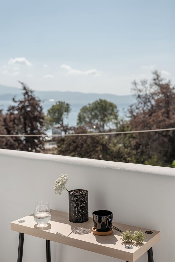A balcony with a table holding a glass, a metal cup, and a small plant. - BY THE SEA (Agia Anna)