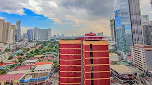 A cityscape with high-rise buildings, a prominent red building in the foreground, and a mix of commercial and residential structures. - TadaiManila Citadel Inn Makati (Makati City)