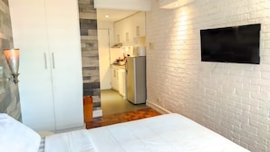 A bedroom with a bed, a TV mounted on the wall, a wardrobe, and a kitchen in the background. - TadaiManila Citadel Inn Makati (Makati City)
