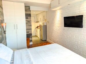 A bedroom with a bed, a TV mounted on the wall, a wardrobe, and a kitchen in the background. - TadaiManila Citadel Inn Makati (Makati City)