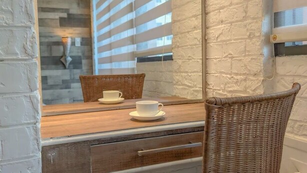 A dining area with a wooden table, wicker chairs, a mirror, and a stone wall. - TadaiManila Citadel Inn Makati (Makati City)