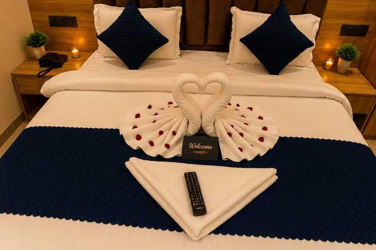 A neatly made bed with a heart-shaped towel arrangement, a welcome card, and a remote control on a blue and white bedspread.