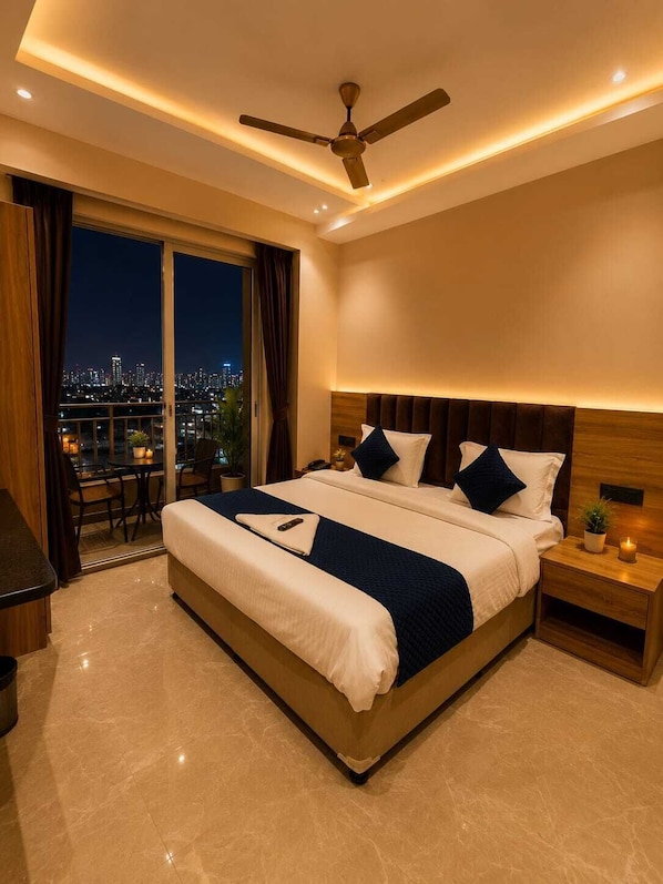 A modern hotel room with a large bed, a ceiling fan, a nightstand, and a view of the city at night.