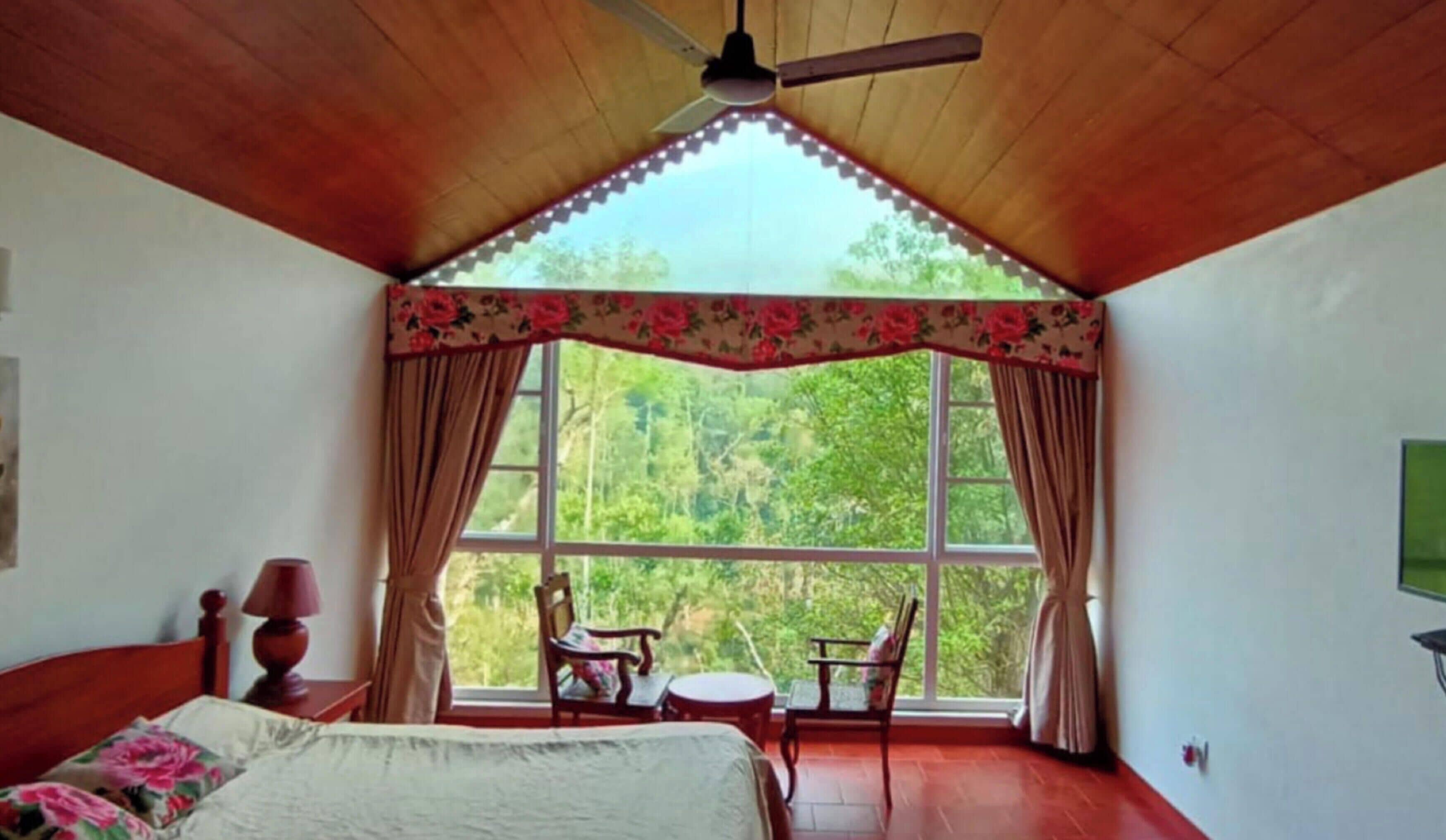 A bedroom with a large window, a ceiling fan, a bed, a chair, and a small table.