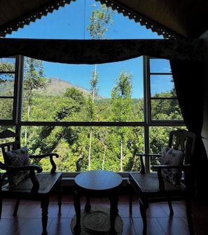 A room with a large window, two chairs, a small table, and a view of a forested area.