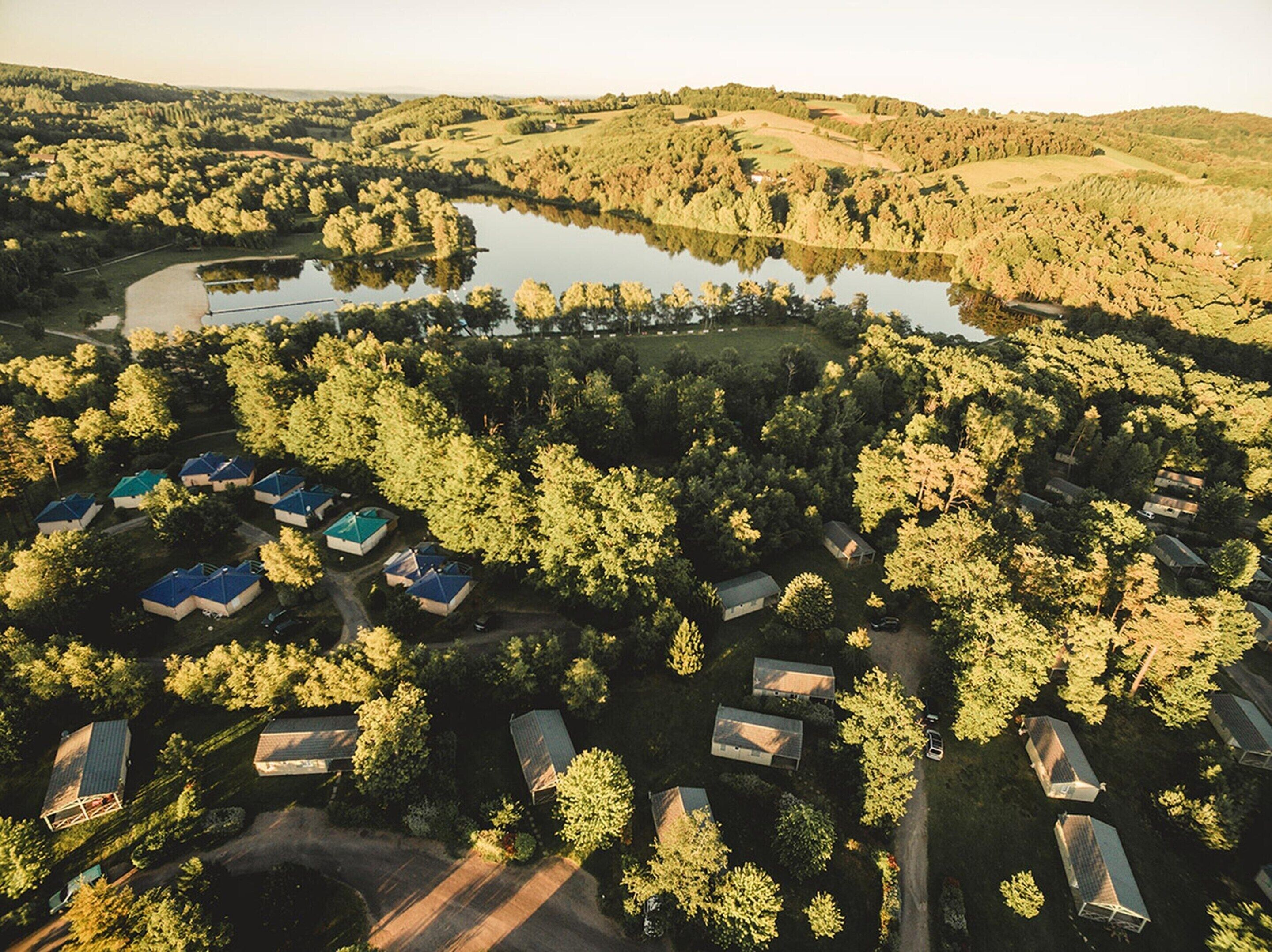 An aerial view of a campground with multiple cabins, a lake, and surrounding forested hills.