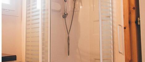 A glass-enclosed shower stall with a white toilet, wooden ceiling, and a small shelf unit.