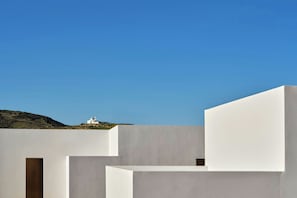 A modern architectural structure with white walls and a flat roof, featuring a small white building in the background.
