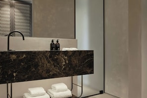 A modern bathroom with a marble sink, two bottles of shampoo, and neatly folded towels. - Orosea, Paros, Autograph Collection (PAROS)