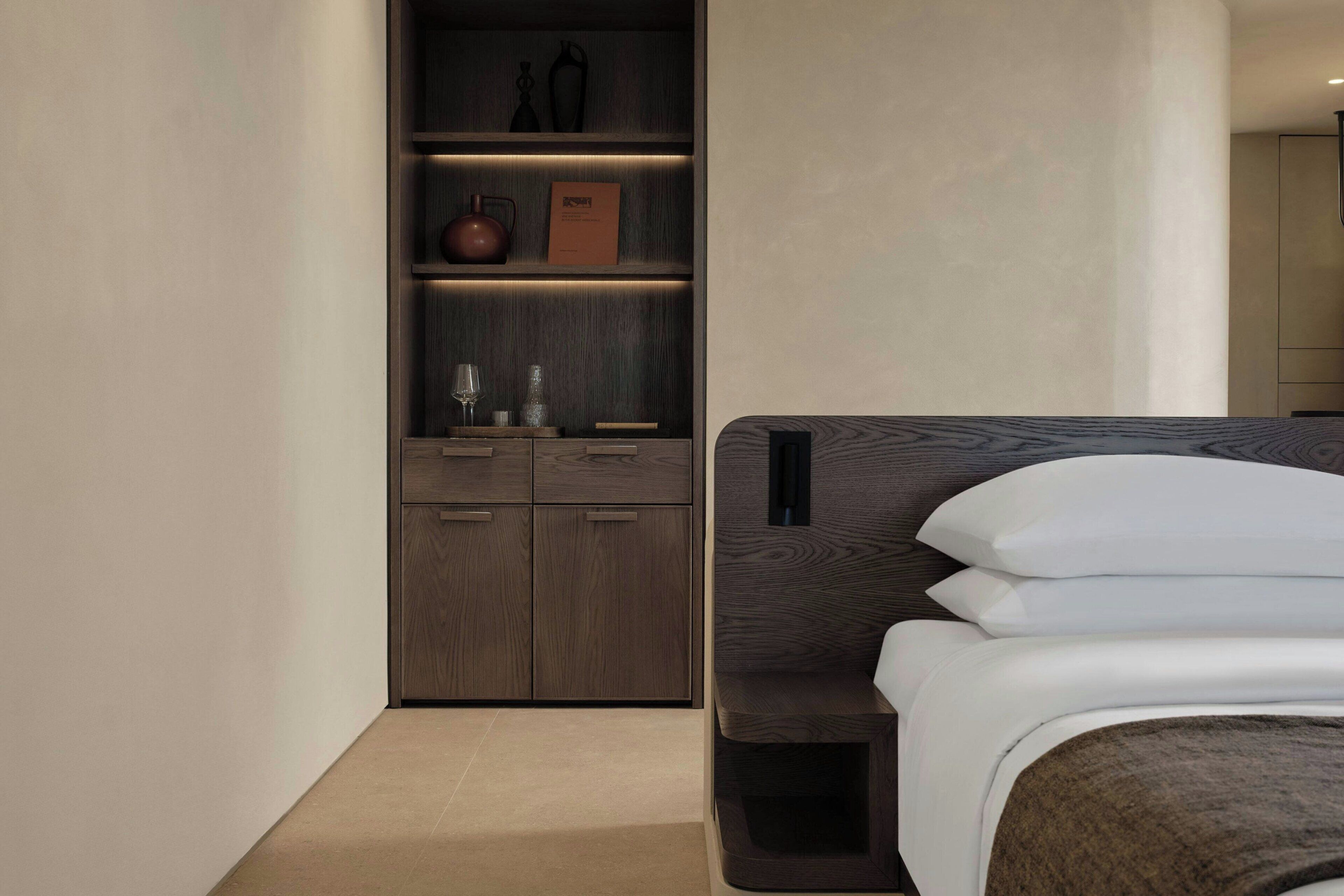 A modern hotel room with a bed, built-in shelving, and a minimalist design.