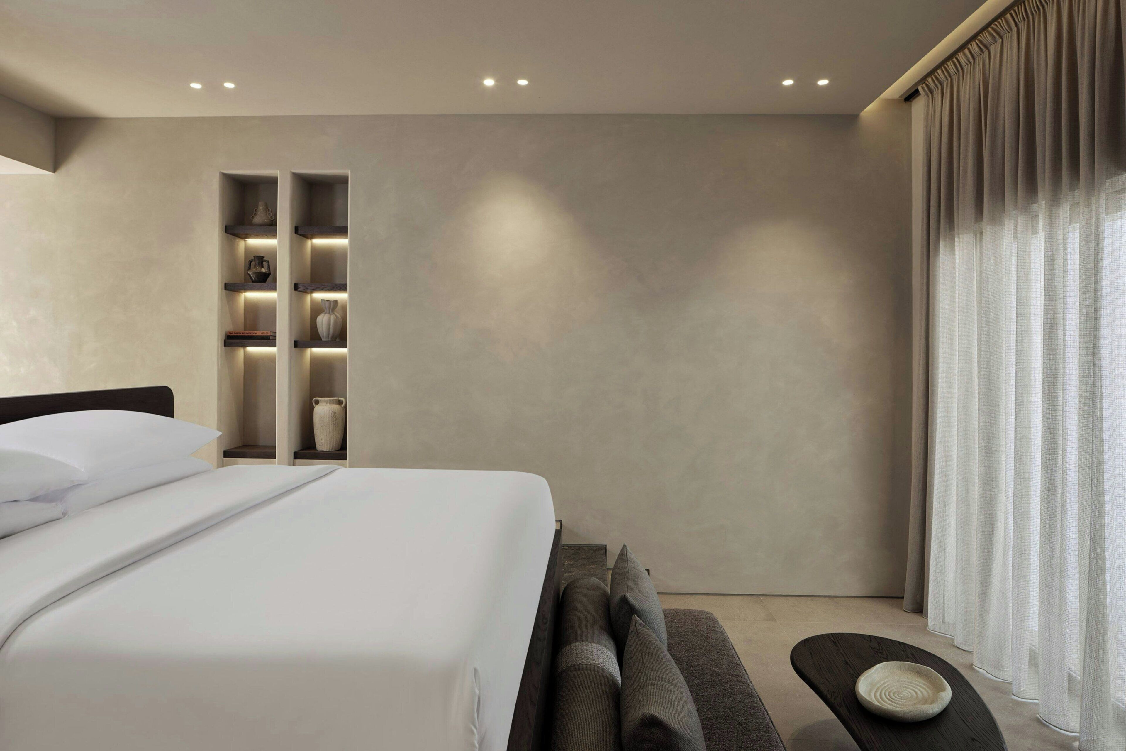 A modern hotel room with a large bed, built-in shelves, and a view of the outdoors.