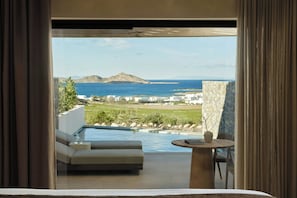 A modern outdoor seating area with a pool, a stone wall, and a view of the sea and distant land. - Orosea, Paros, Autograph Collection (PAROS)