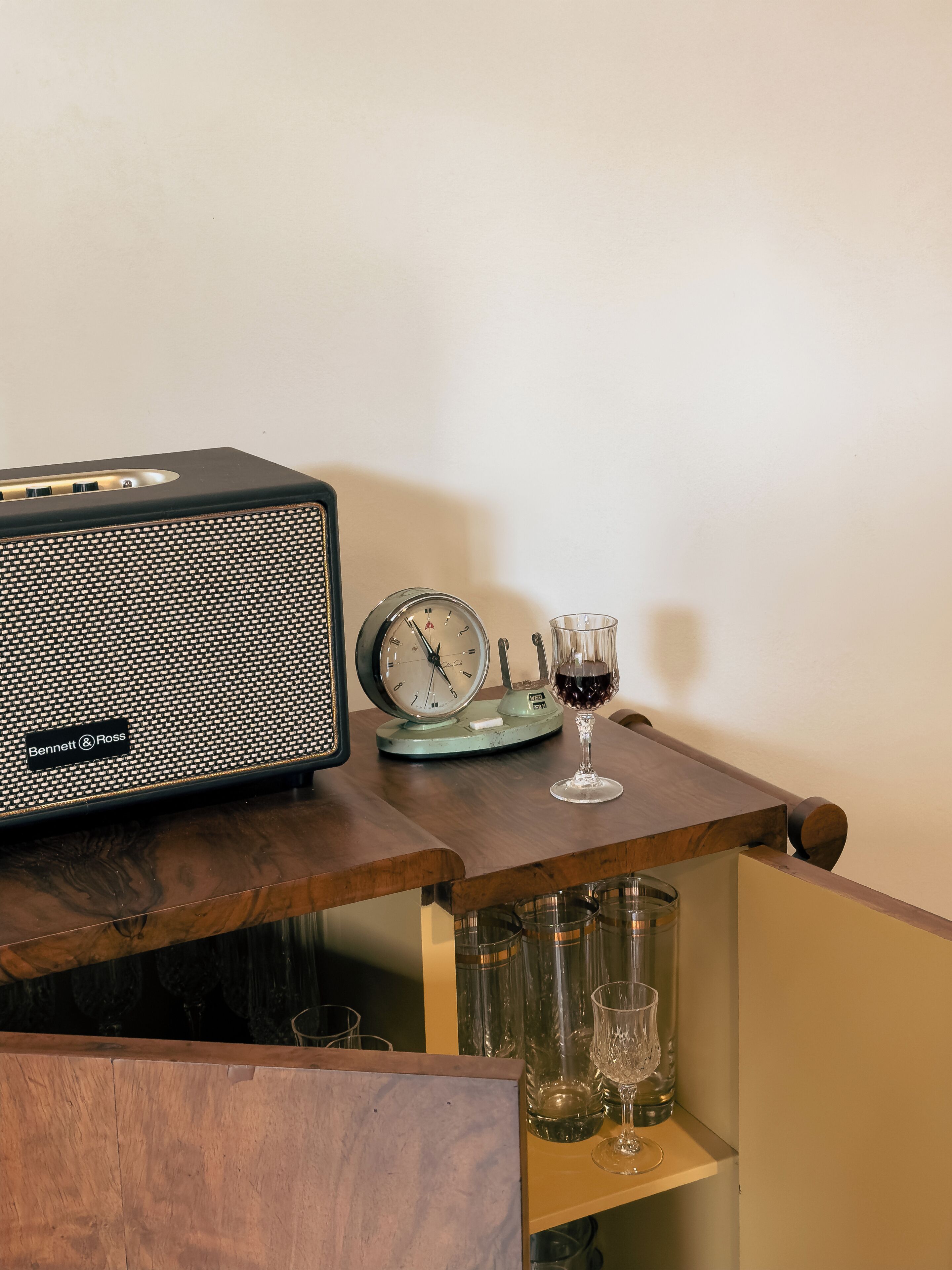 Una mesa de madera con una radio antigua, un reloj y una copa de vino.