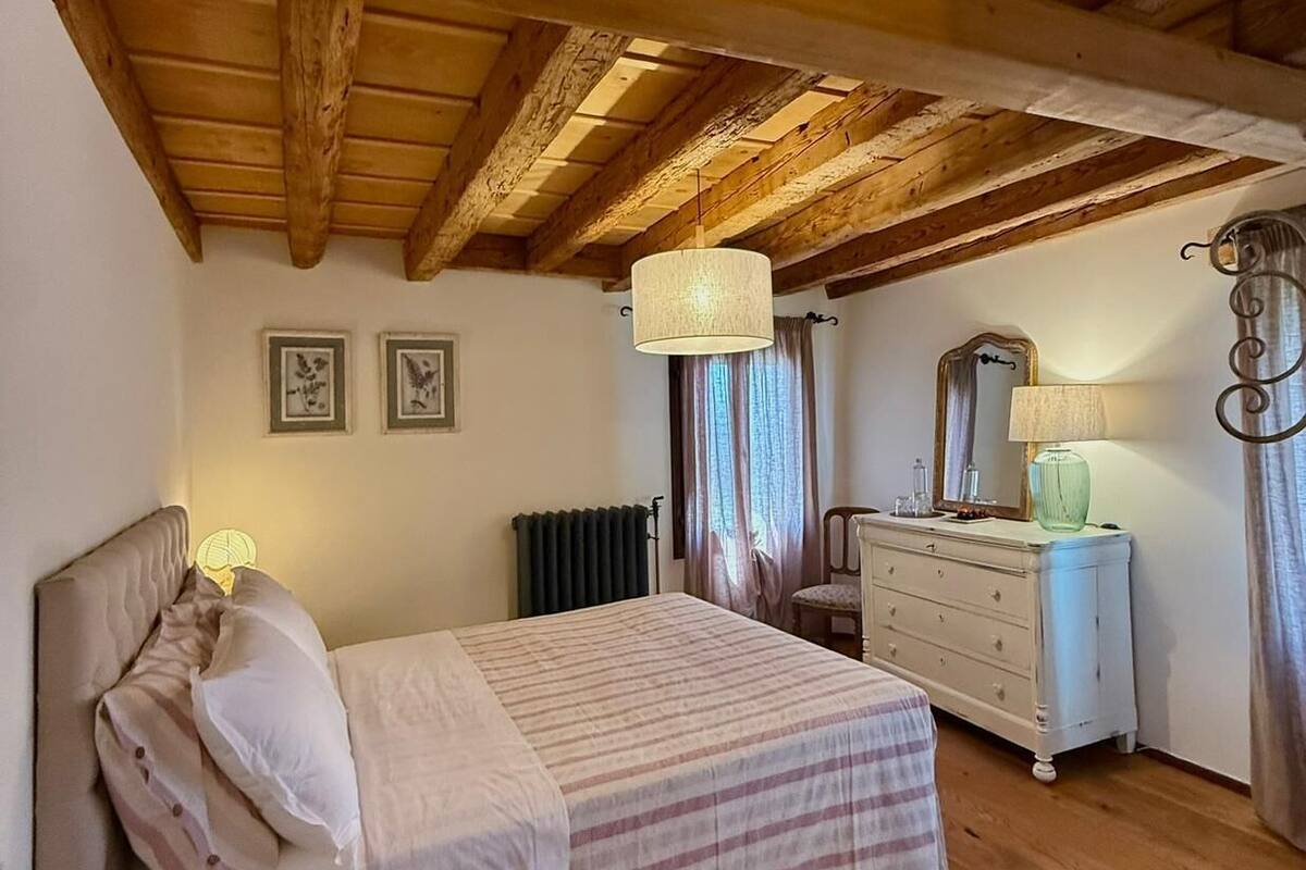 Un dormitorio con techo de madera, una cama con colcha a rayas, un aparador, un espejo y dos cuadros en la pared.