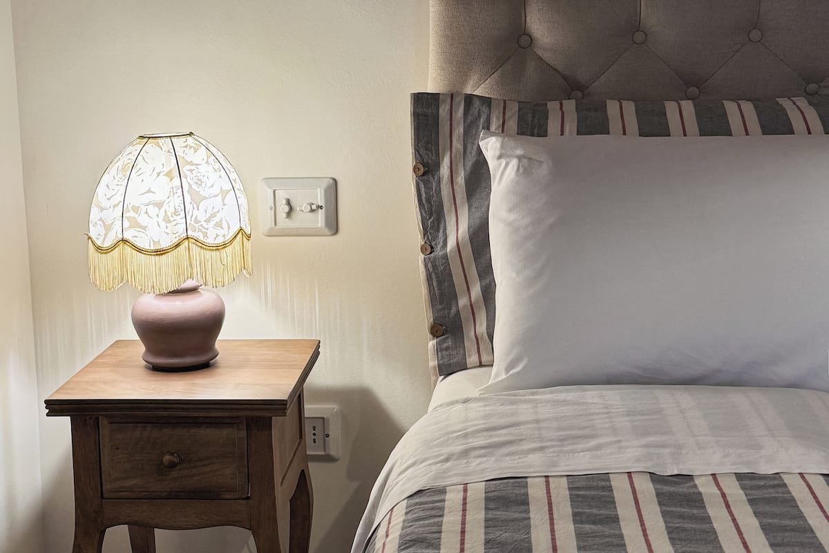 Una cama con ropa de cama a rayas, un cabecero y una mesita de noche con una lámpara.