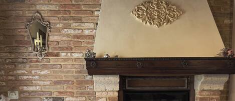 A brick fireplace with a mantel, a wooden table, and a wicker chair in a room with a brick wall.