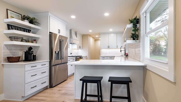Una cocina moderna con armarios blancos, electrodomésticos de acero inoxidable y una isla central con dos taburetes.